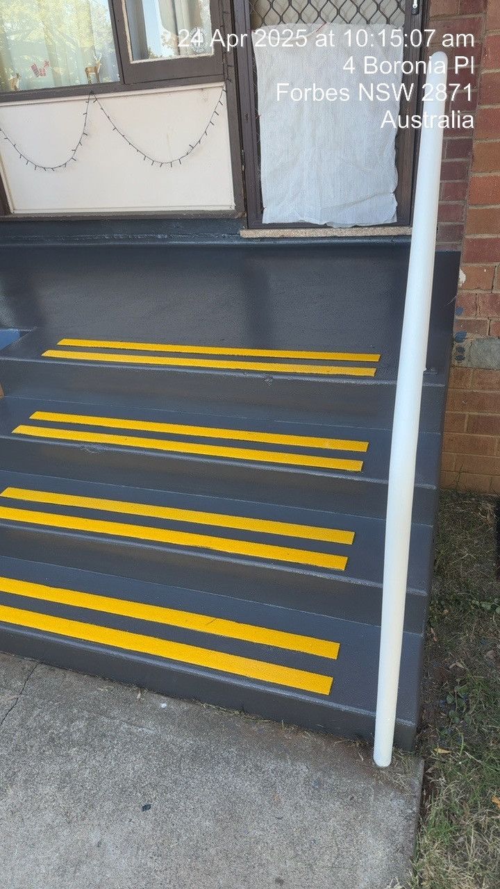 Black front steps with yellow safety stripes and a white handrail outside a building.