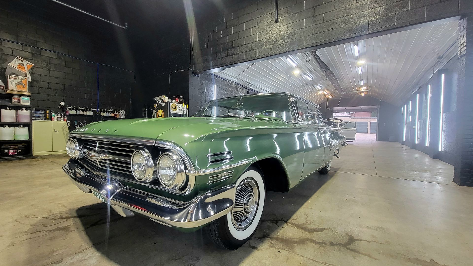 Green classic lowrider car parked indoors in a warehouse-style garage, front-left view.