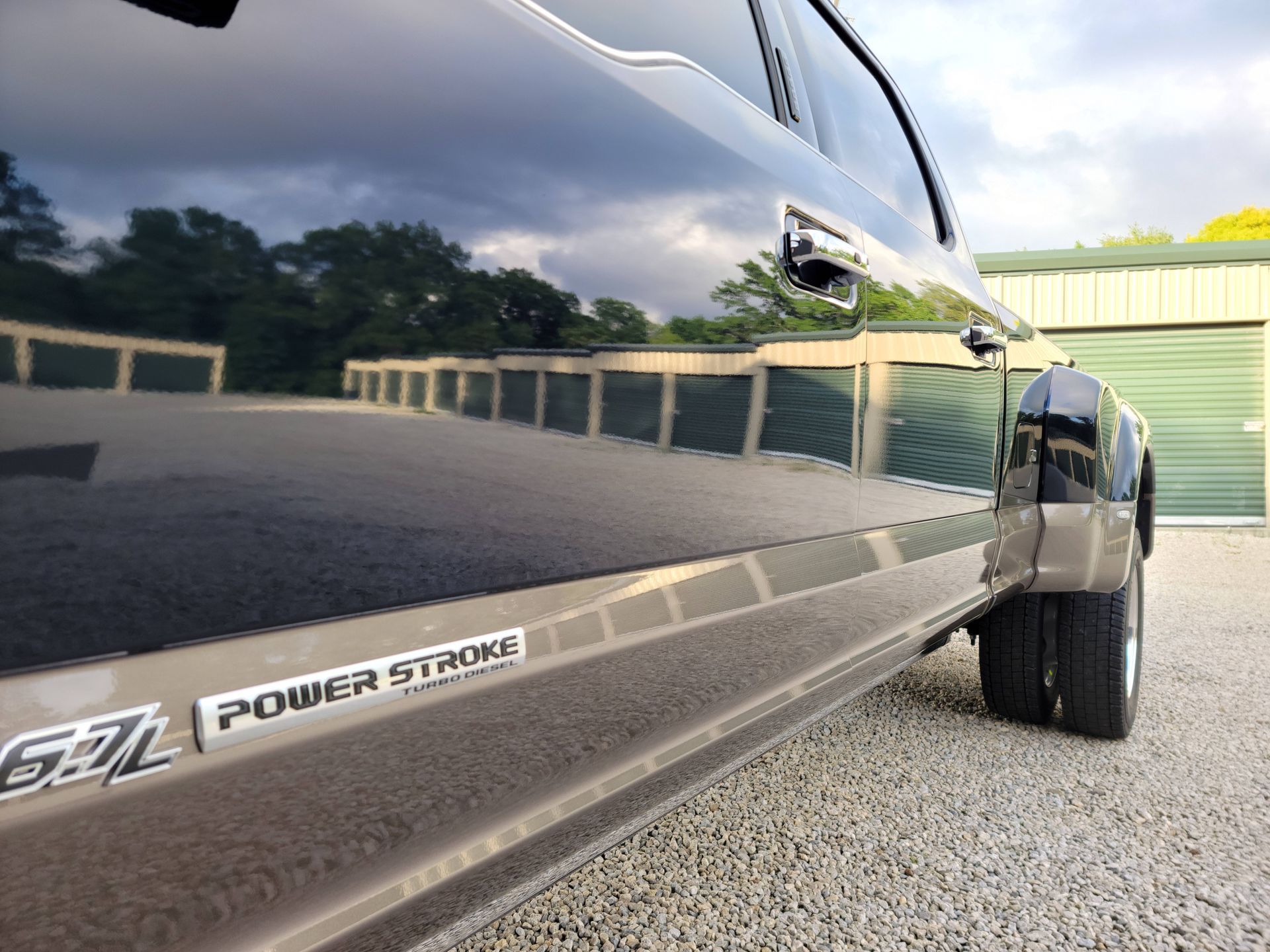 Close-up of a black Ford F-350 Power Stroke truck parked on gravel beside a building.