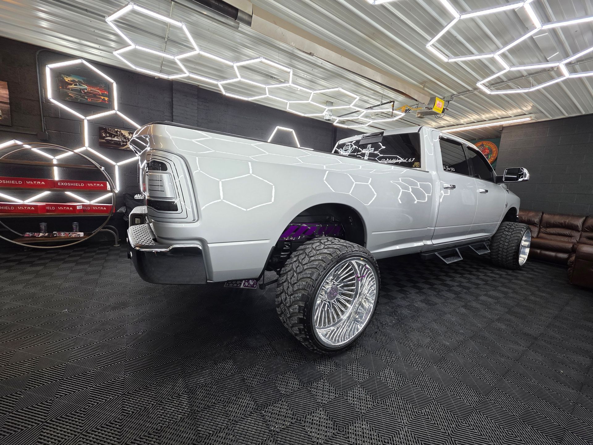 White lifted pickup truck with chrome rims in a showroom under hexagonal ceiling lights