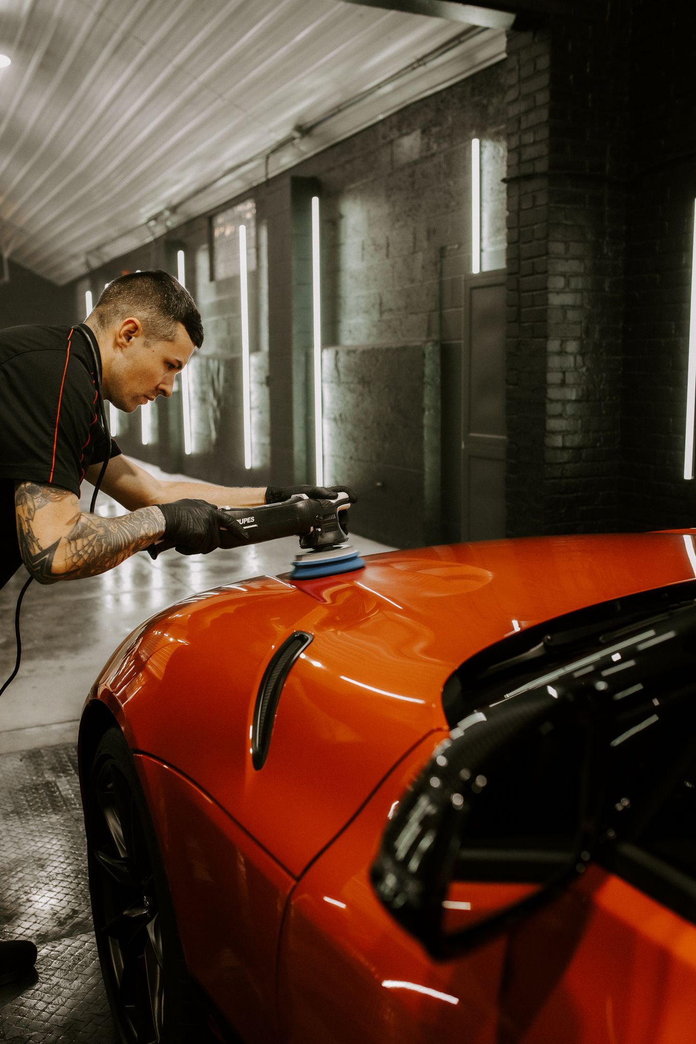 Mechanic polishing a bright orange sports car in a garage