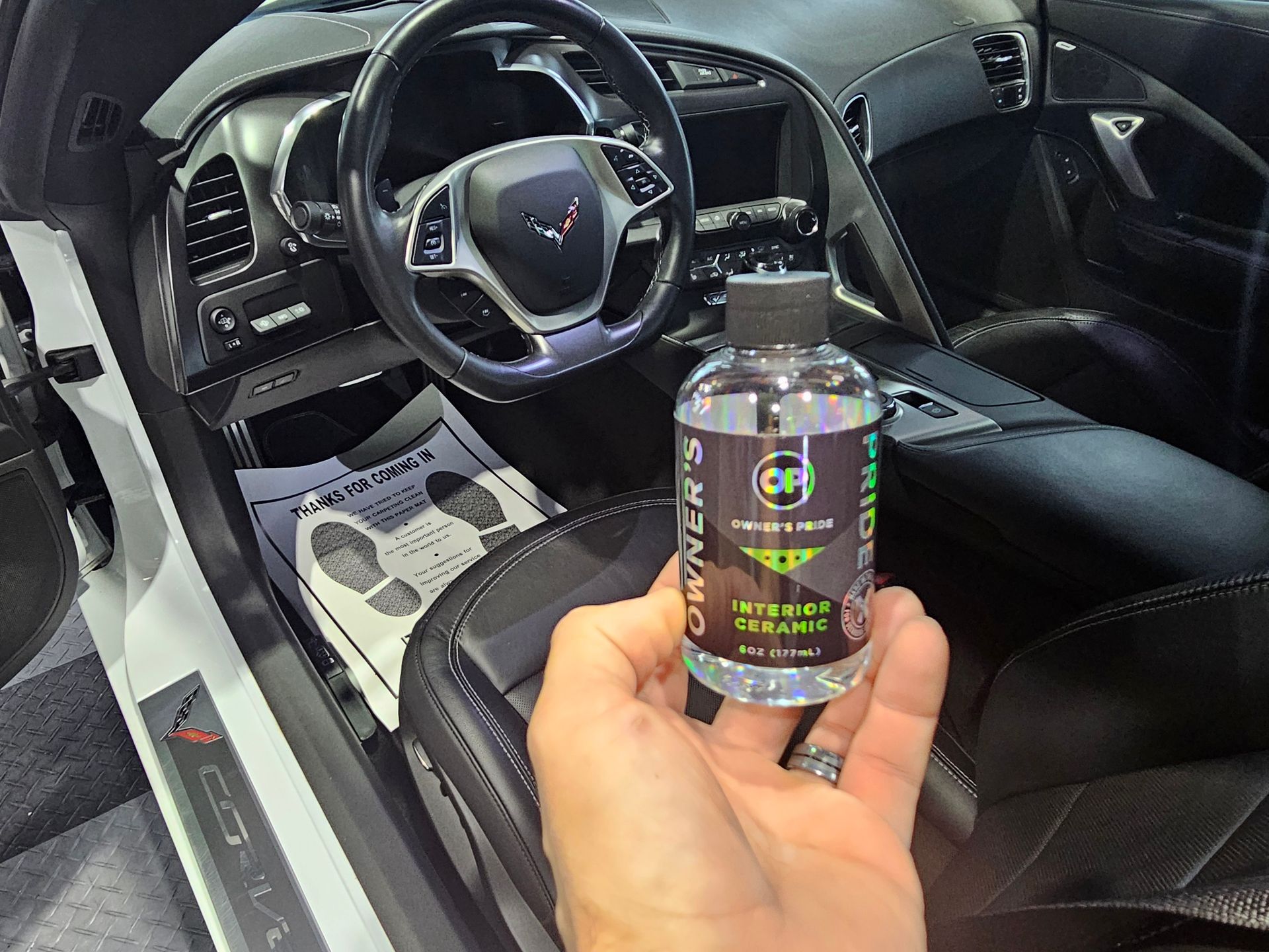 A person is holding a bottle of cleaner in front of a car.