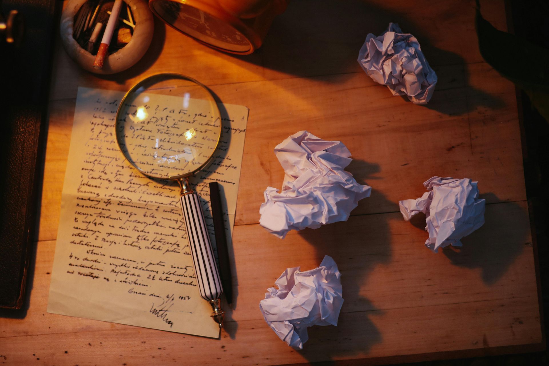 A magnifying glass on a sheet of handwritten paper with screwed-up paper round it.
