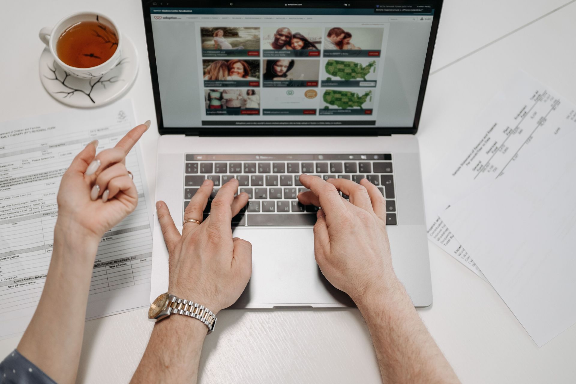 An open laptop with two hands typing and one pointing at the screen