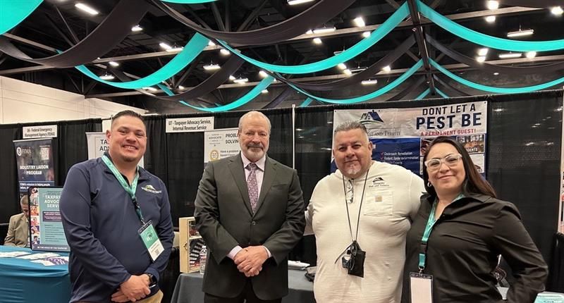 Four people posing at a trade show booth with black displays and teal hanging ribbons