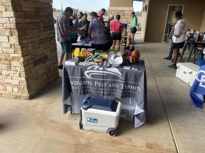 Outreach table with snacks and drinks under a covered walkway, people gathered around it