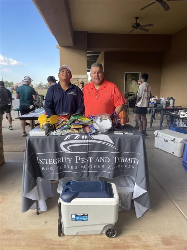 Two people behind a table at an outdoor pet and termite service booth with flyers and a cooler