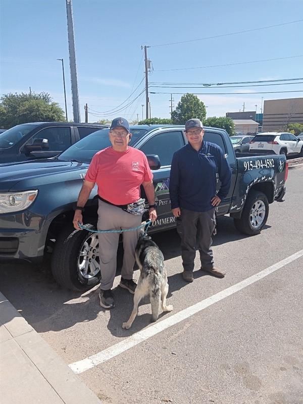 Two people standing beside a black police pickup truck with a police dog on a road.
