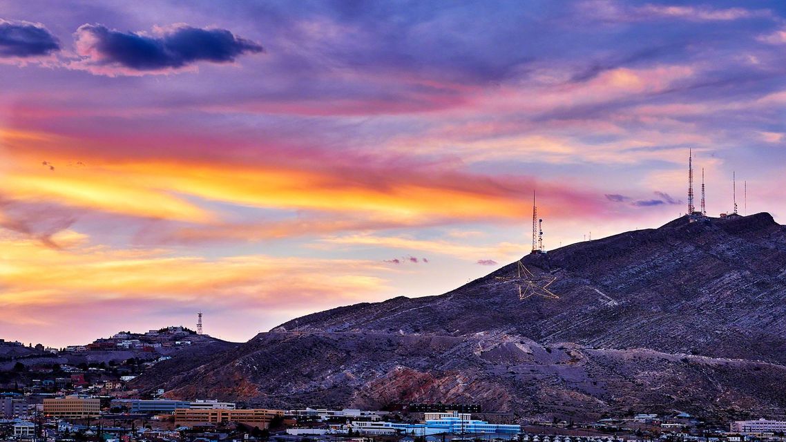 Purple and pink sunset over a rocky hill with radio towers above a city skyline
