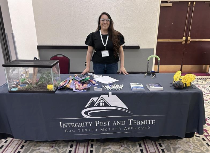 Vendor booth for Integrity Pest and Termite, with a woman behind a table displaying brochures and a terrarium.