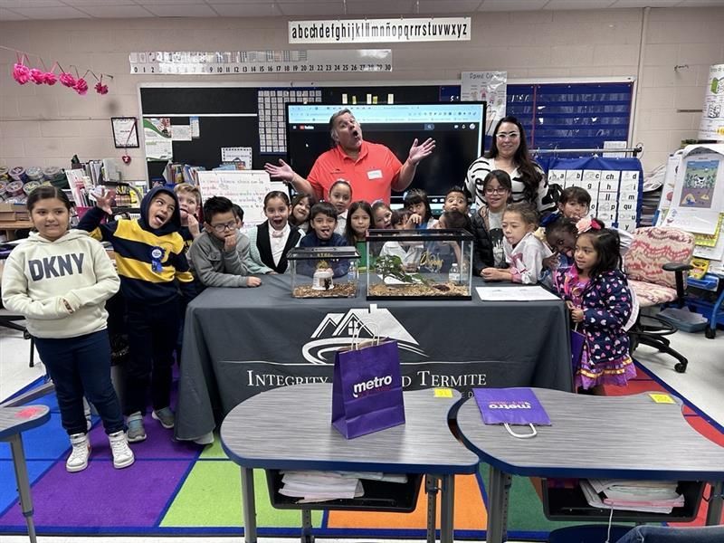 Classroom group posing around a table with a man and children behind a display case and black tablecloth