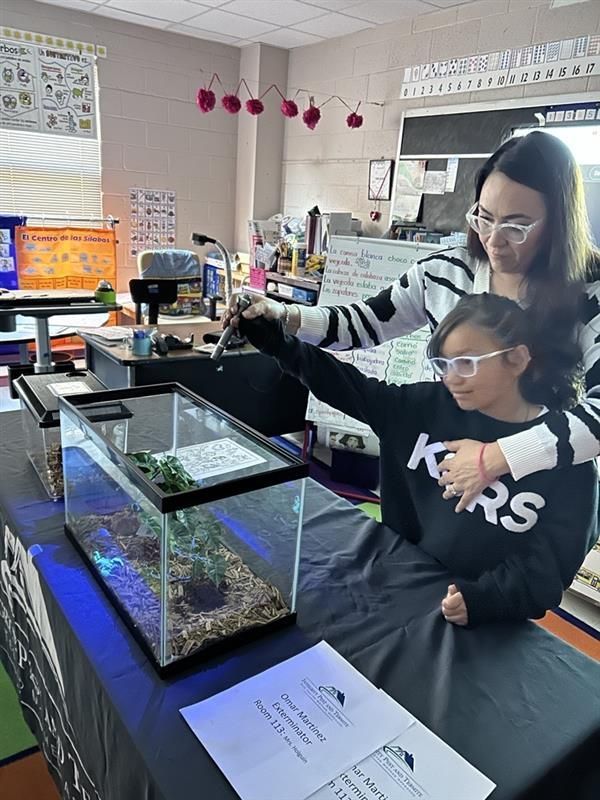 Adult and child feeding a fish tank in a classroom with science materials and posters