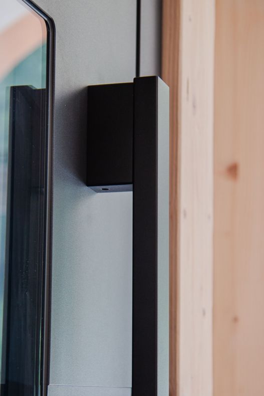 Cerniera nera a parete accanto a un telaio di porta in legno e un pannello di vetro