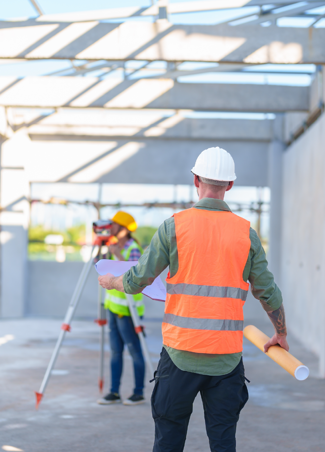 A construction worker is standing on a construction site holding a blueprint.