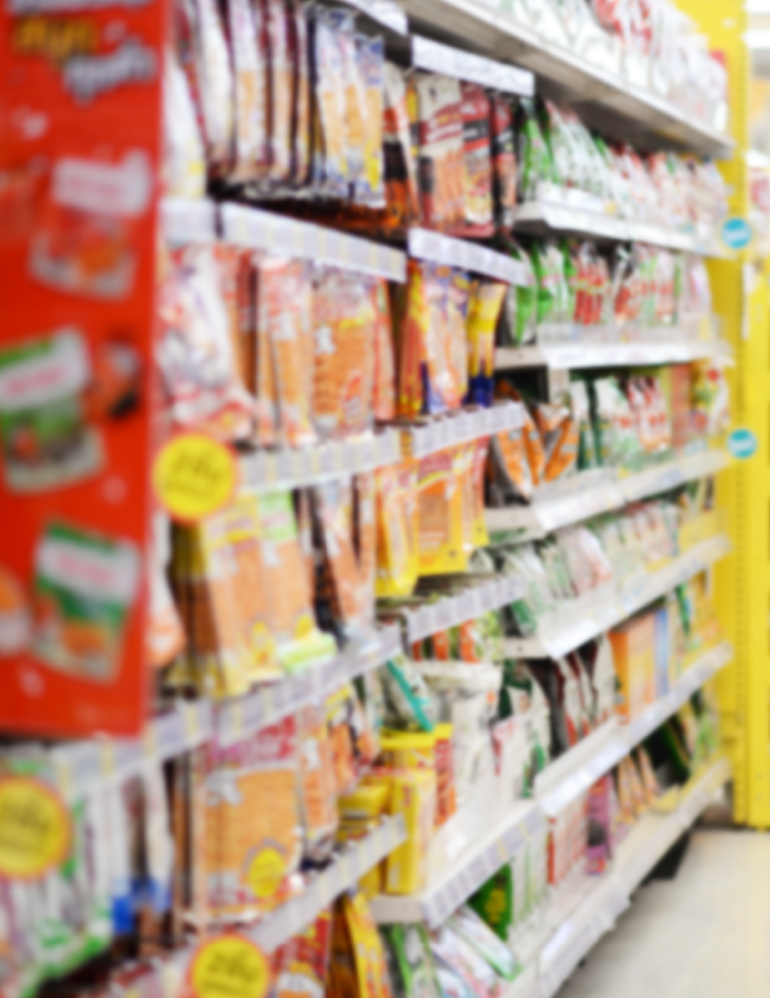 A blurred image of a grocery store aisle filled with bags of food.