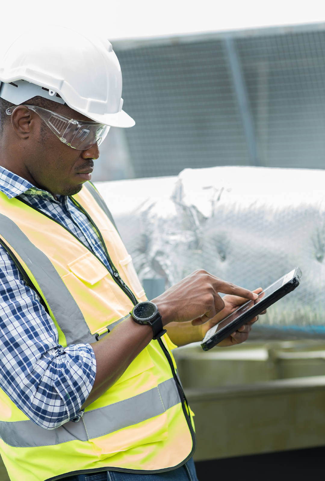 A man wearing a hard hat and safety vest is using a tablet computer.
