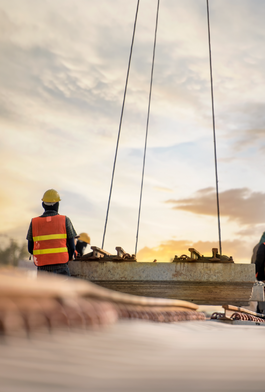 A construction worker is standing next to a crane at a construction site.