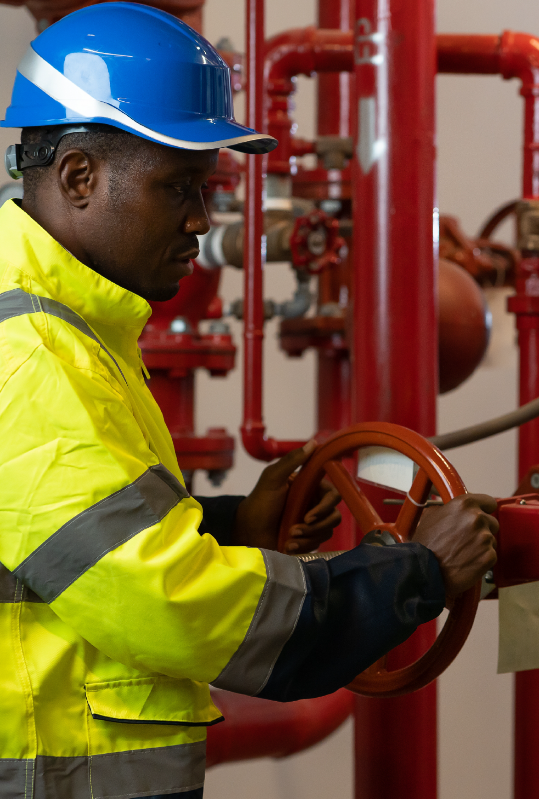 A man wearing a blue hard hat and a yellow jacket is working on a valve.