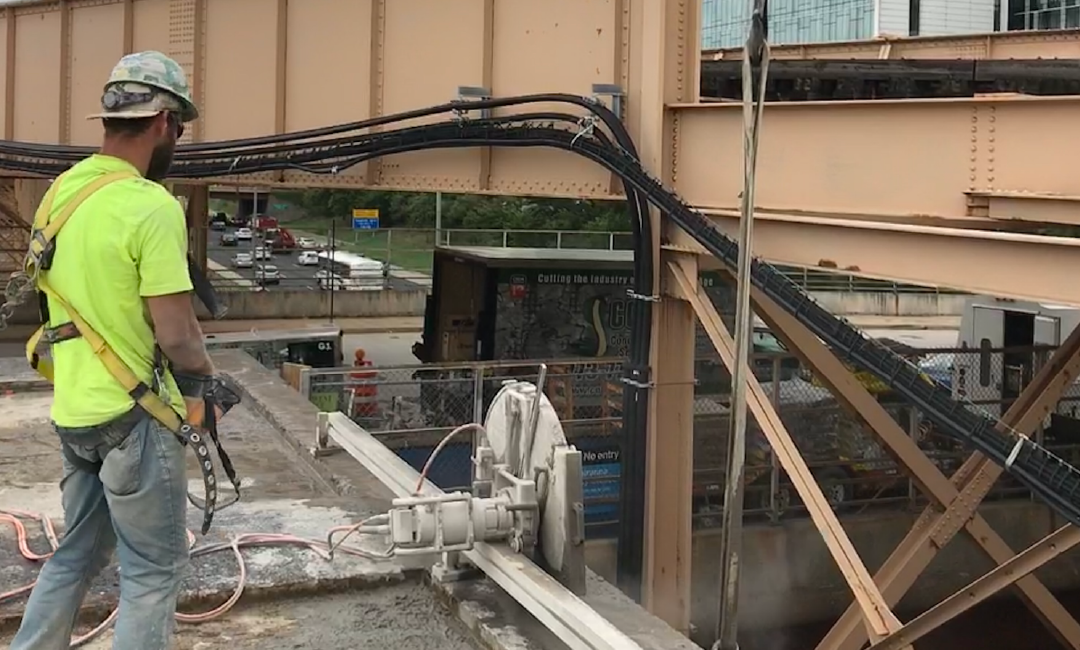 A man is cutting concrete with a machine on a bridge.