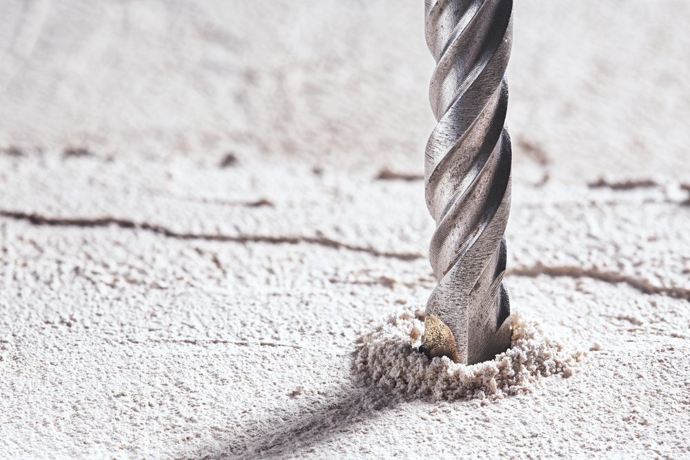 A close up of a drill bit making a hole in a concrete wall.