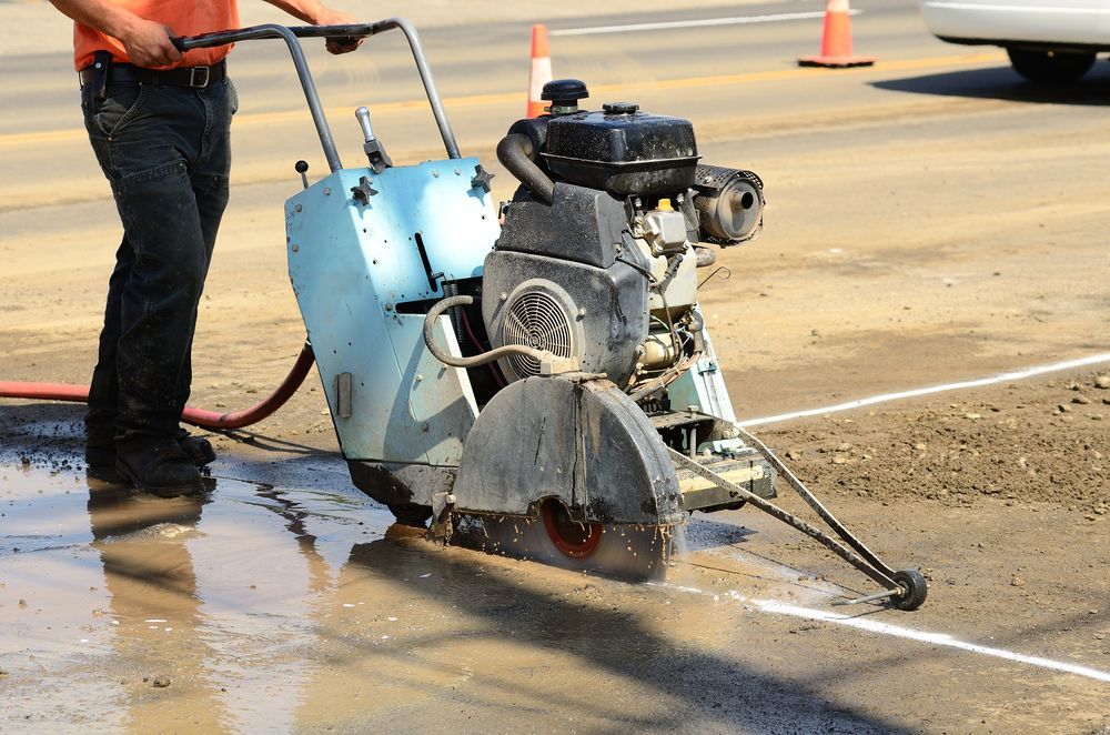 A man is using a concrete saw to cut a line on the road.