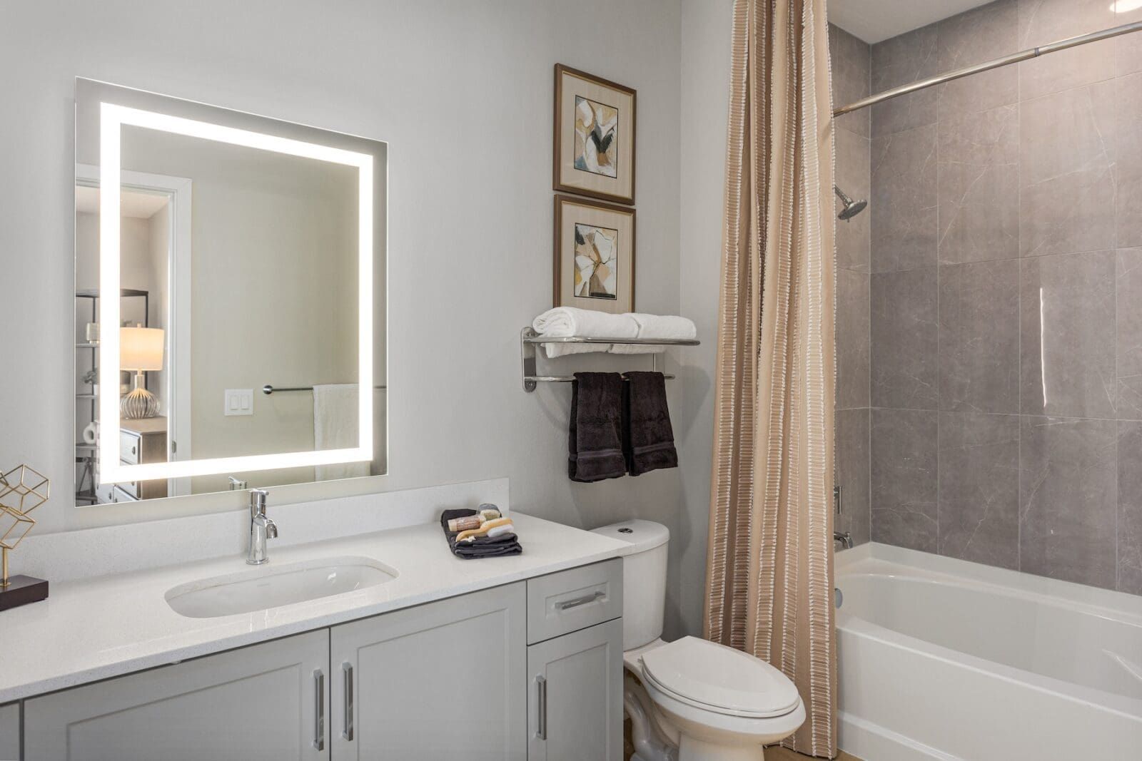 Modern bathroom with a large lit vanity mirror, sink, toilet, and bathtub with shower at Echo Biltmore in Phoenix AZ.