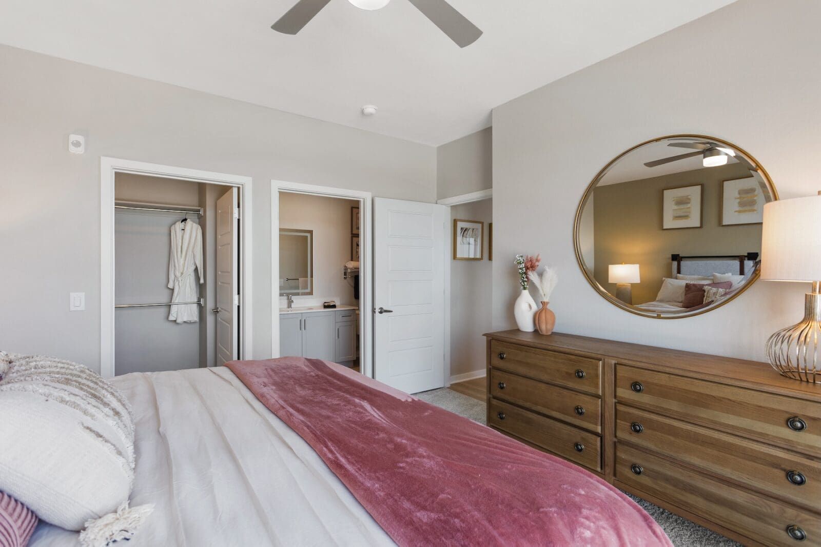 Bedroom with a closet and bathroom access, featuring a dresser and a large round mirror at Echo Biltmore in Phoenix AZ.