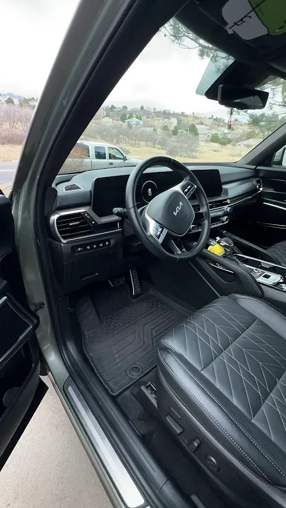 Car interior with black leather seats, steering wheel, and center console, viewed from the open driver’s door