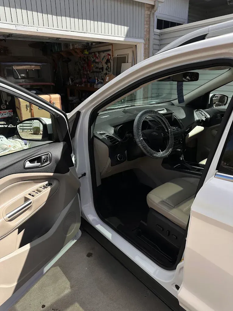 Open white car with driver door ajar in a garage, showing the steering wheel and front seats.