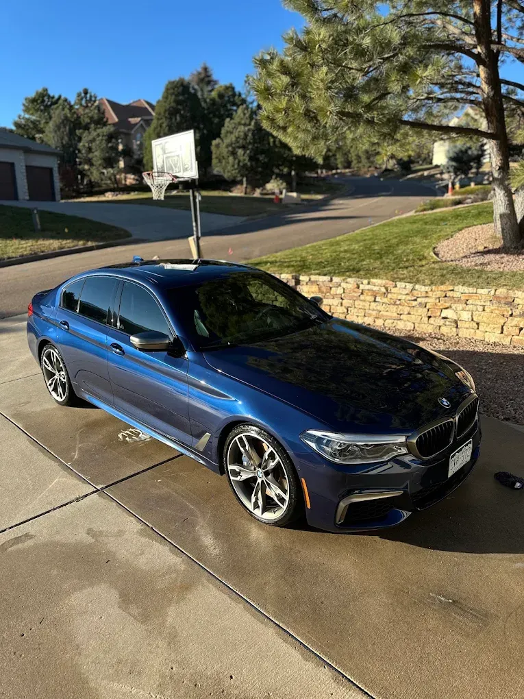 Blue sedan parked on a wet driveway beside a stone wall in a sunny suburban neighborhood
