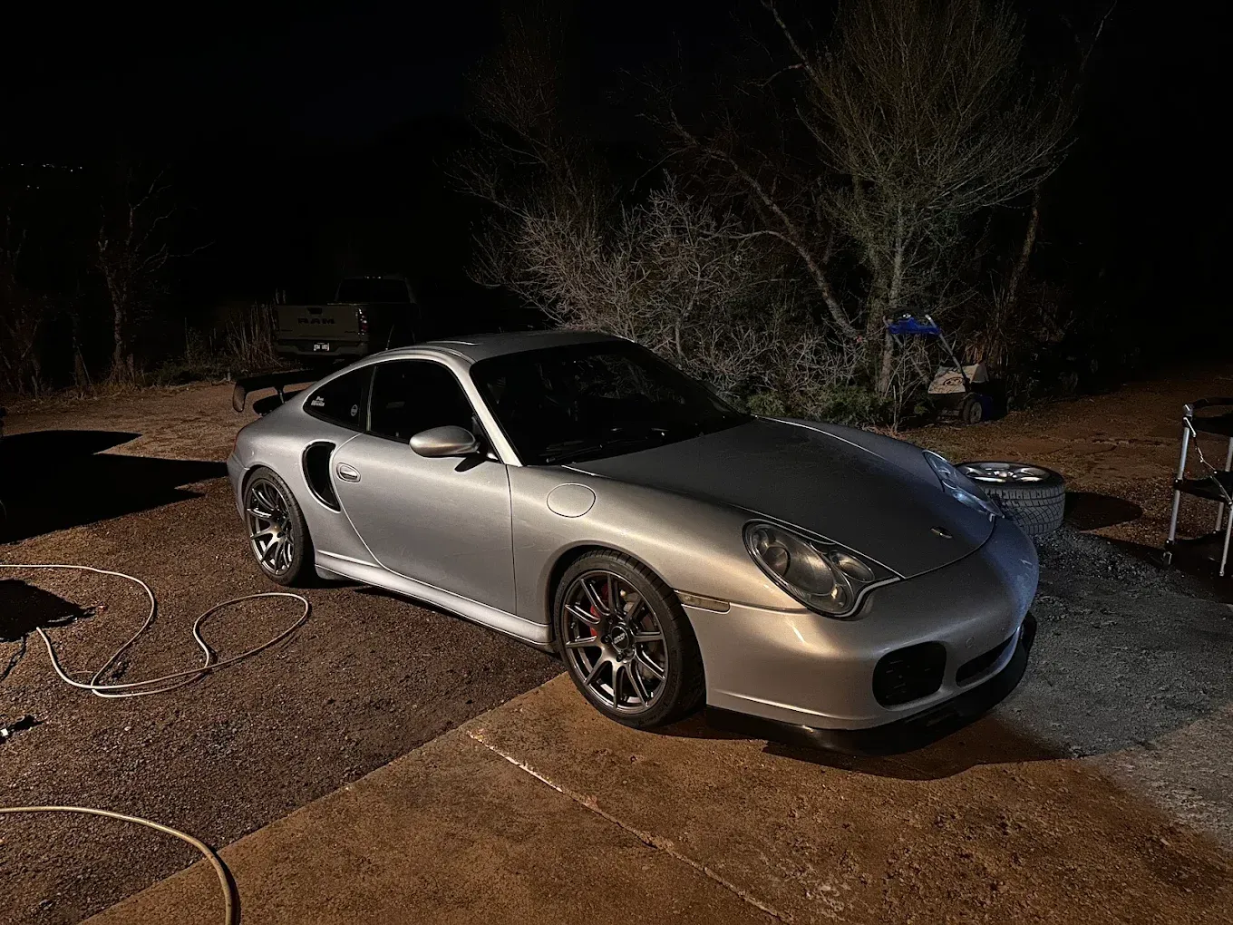 Silver sports coupe parked on a gravel driveway at night, lit by a bright flash.