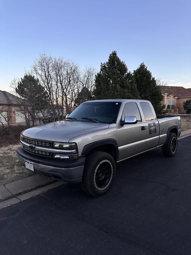 Dark gray pickup truck parked along a suburban street at dusk, with bare trees and houses in the background