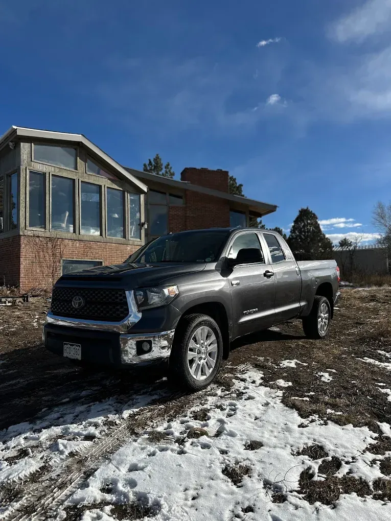 Silver pickup truck parked beside a brick house on a snowy driveway under a blue sky