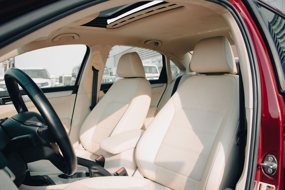 Car interior with beige leather front seats and steering wheel, viewed from the open driver-side door