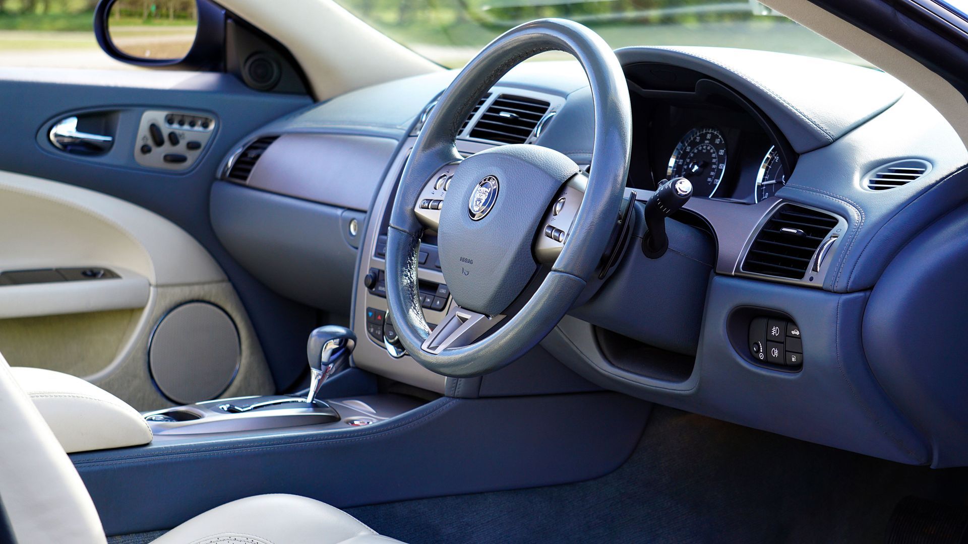 Car interior with blue dashboard, steering wheel, and open driver’s door, showing front seats and controls