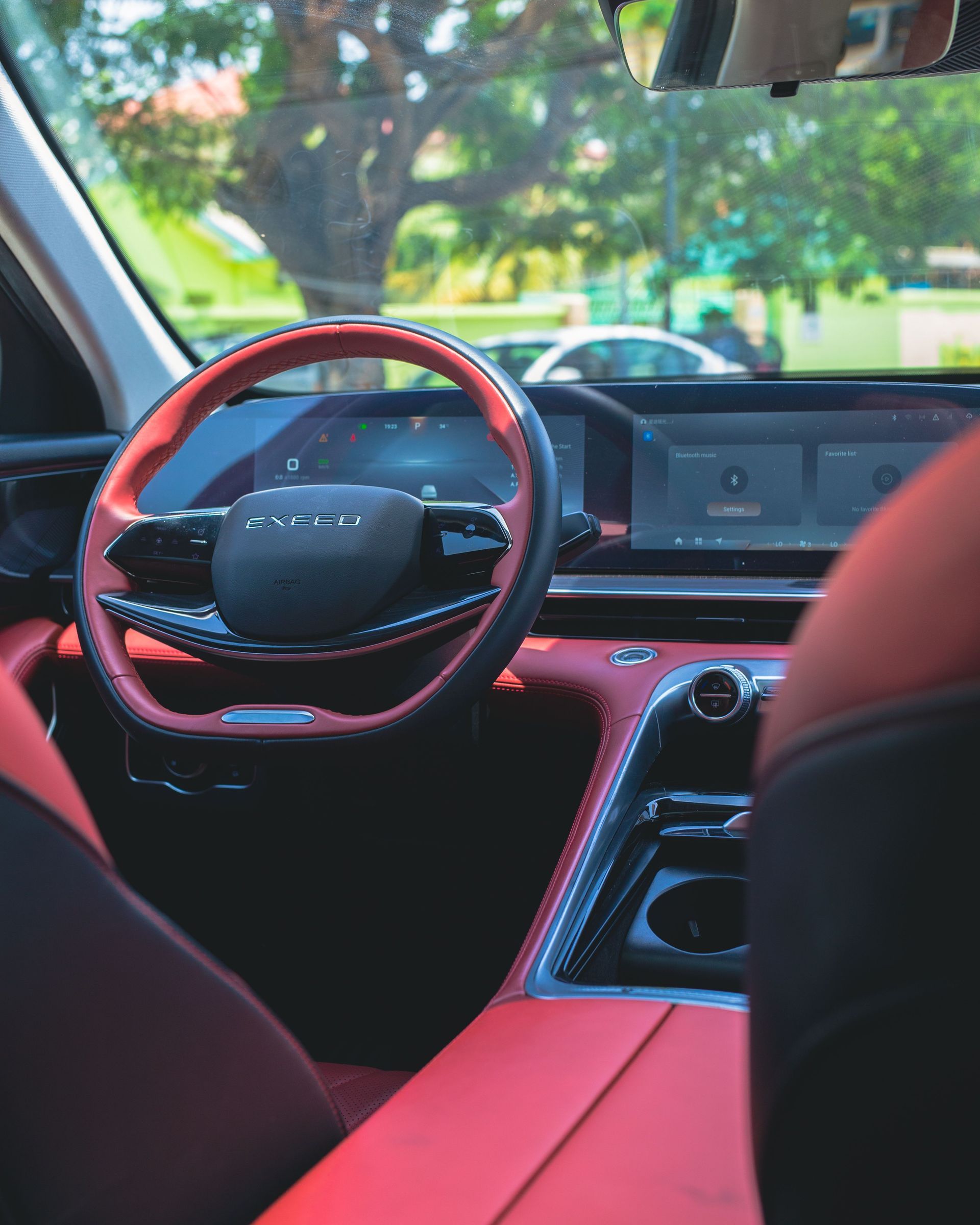 Car interior with red accents, steering wheel, dashboard screen, and front seats in a parked car.