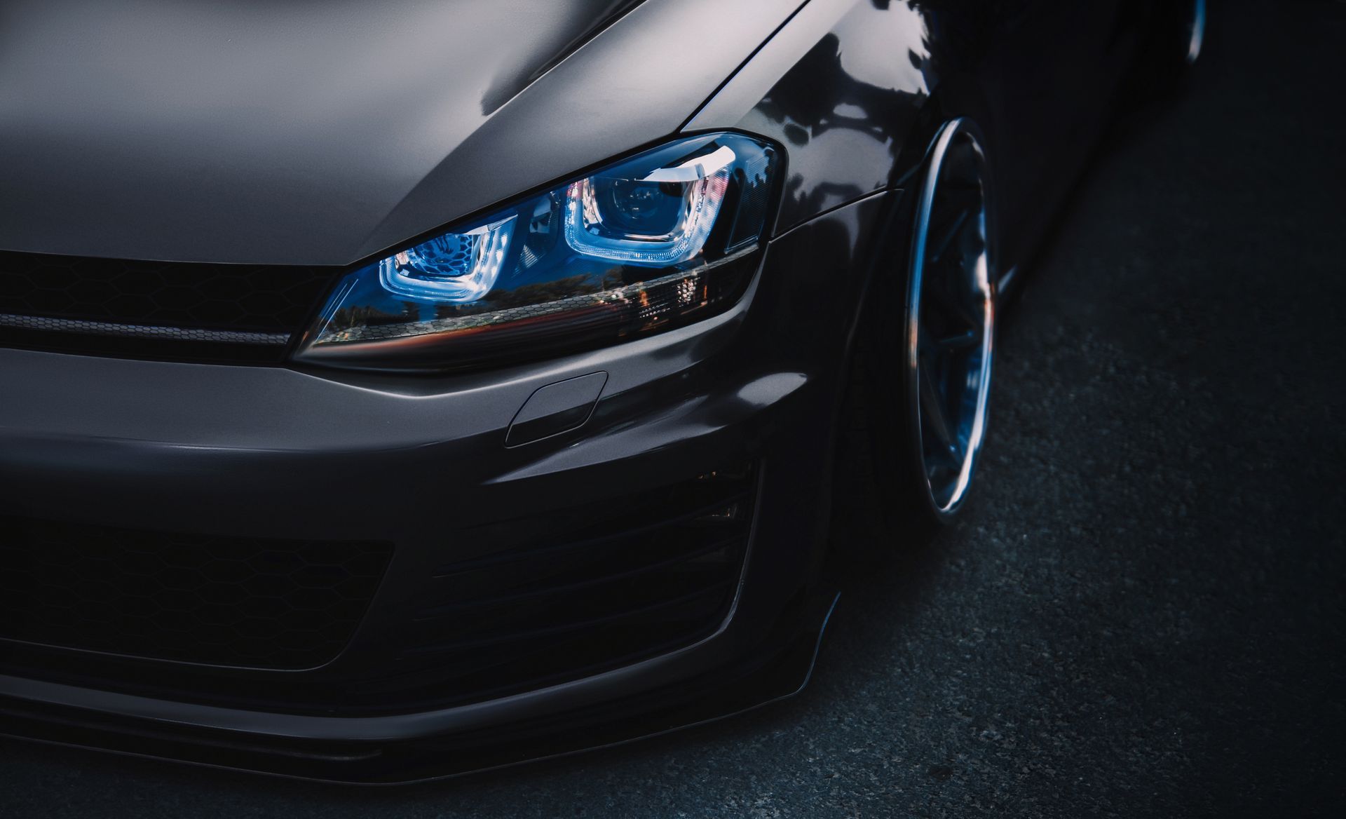 Close-up of a black sports car front end with blue headlights on a dark road