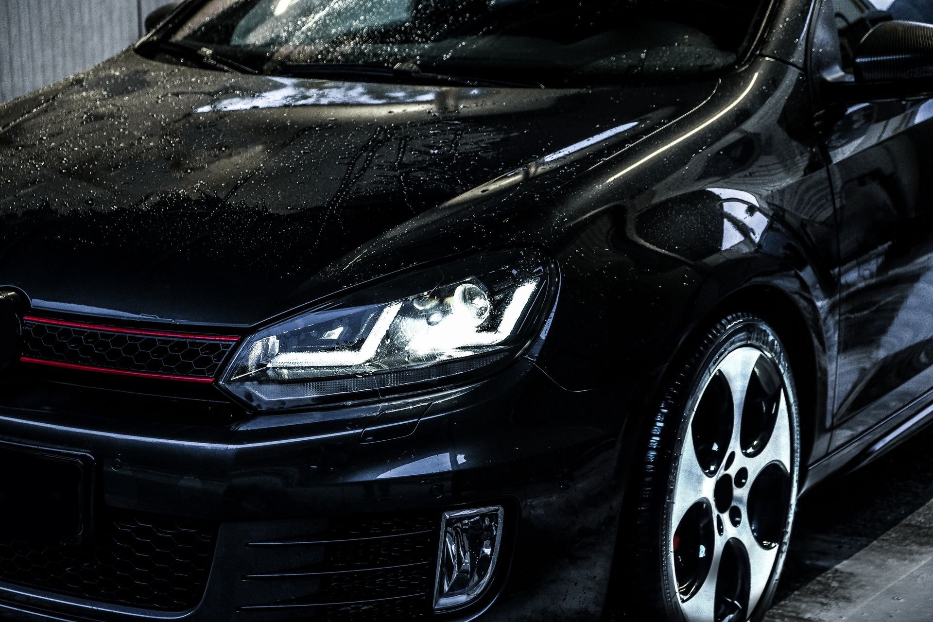 Black sports car with headlights on, wet exterior, parked indoors.