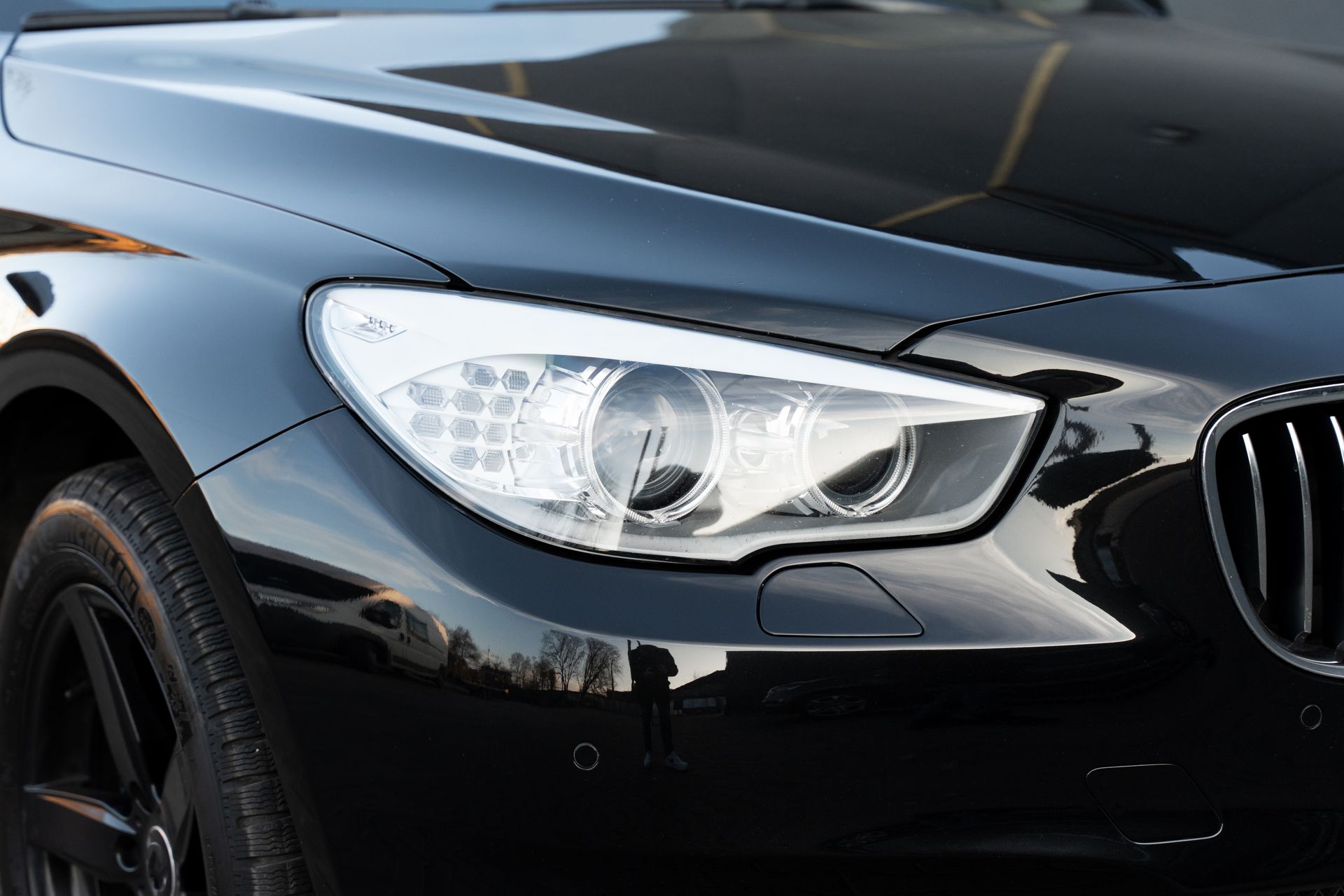 Close-up of a black car’s front headlight and grille with glossy reflections