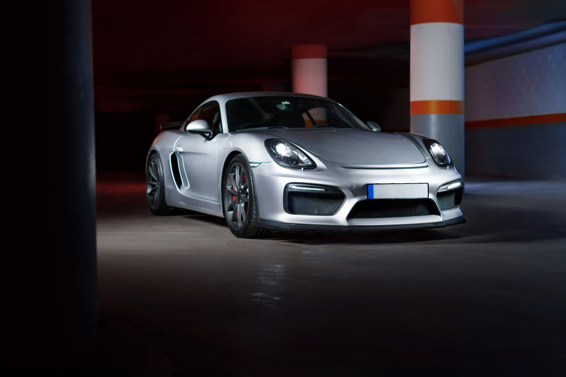 Silver sports car parked in a dim garage with orange-and-white pillars