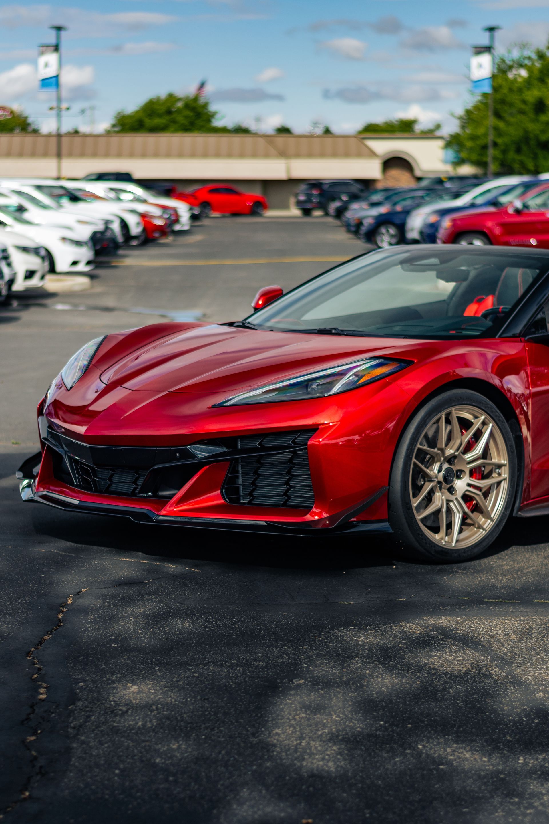 Red sports car parked in a lot between rows of cars on a sunny day
