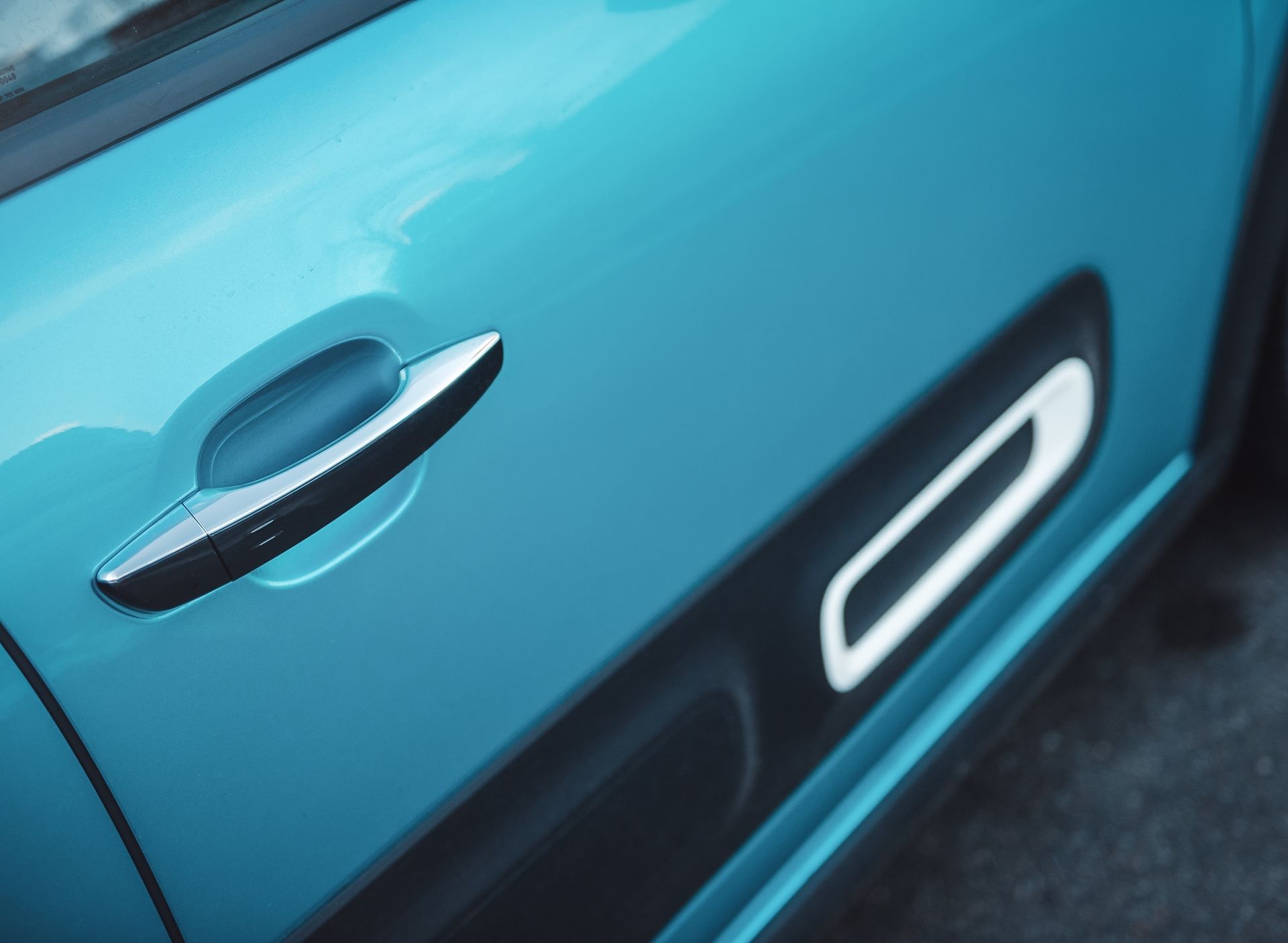 Close-up of a teal car door with a silver handle and black trim.