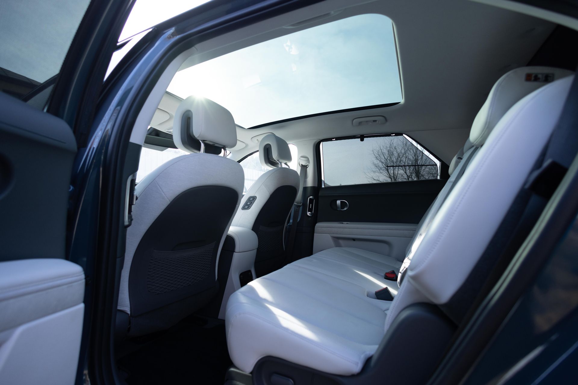 Inside a car’s rear seats, white leather upholstery and an open door reveal the spacious interior.