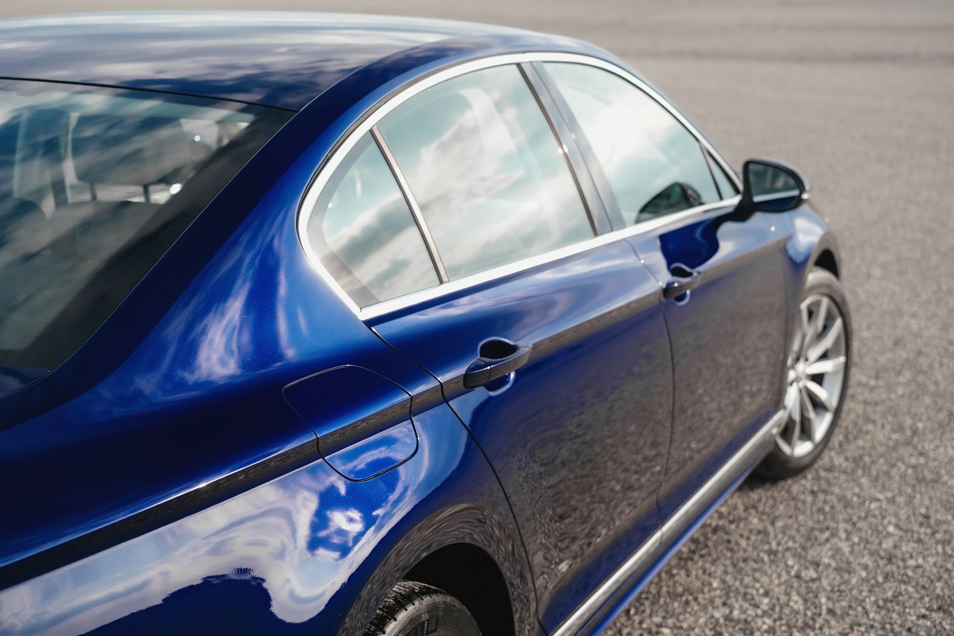 Blue sedan parked on pavement, side view with reflective windows and silver wheel rim