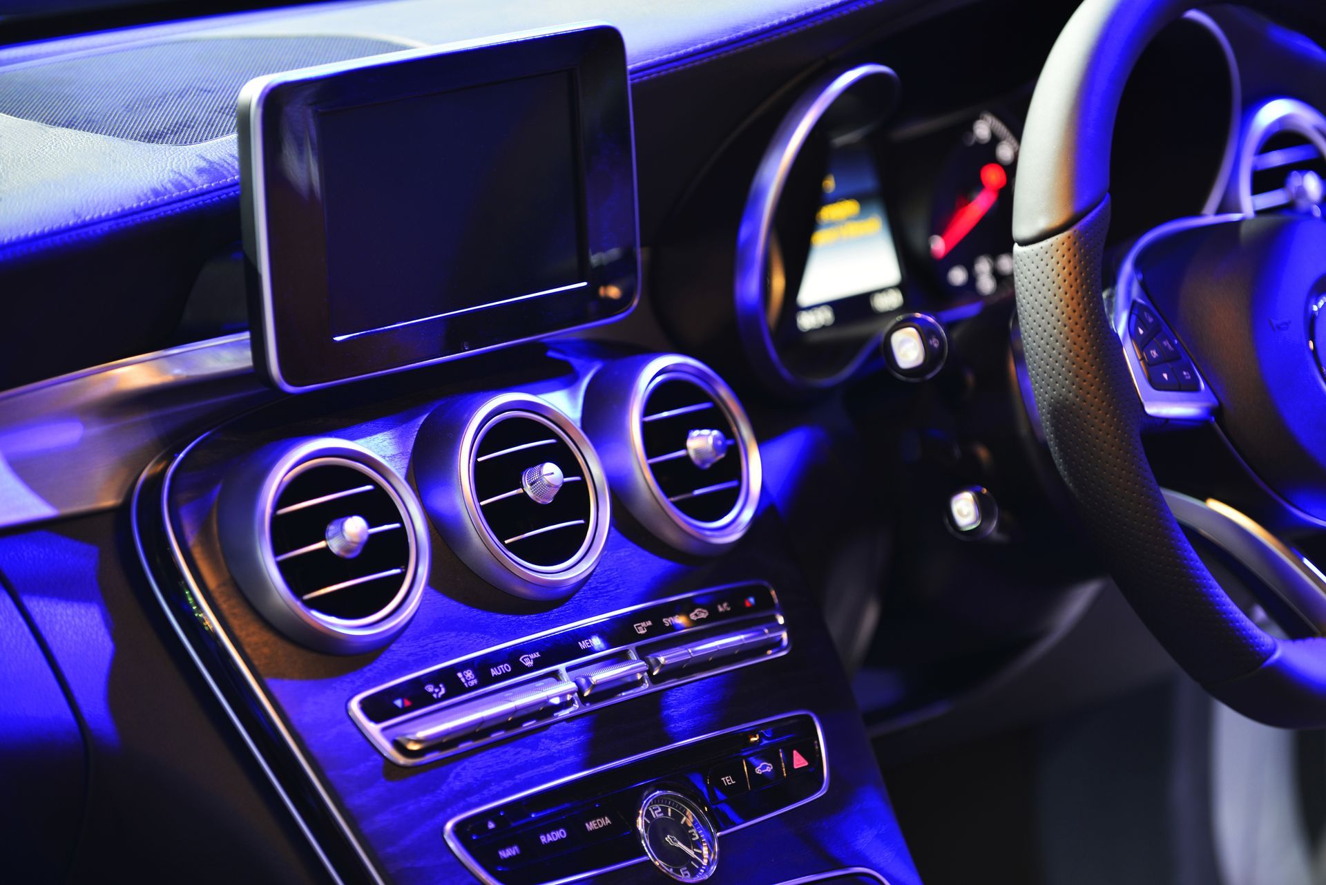 Car dashboard with three round air vents, center display, and illuminated gauges in blue-purple light