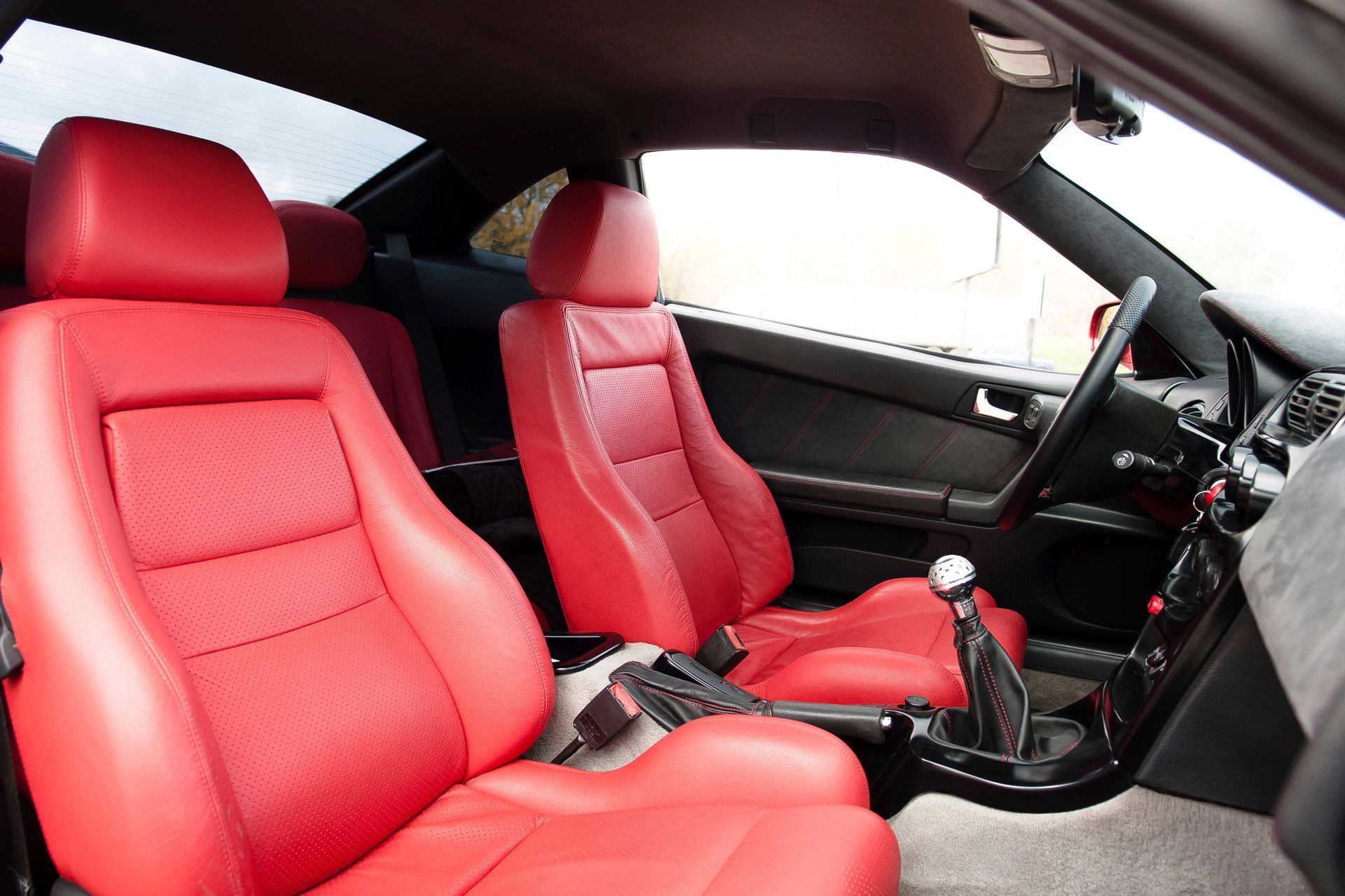 Red leather car seats and manual transmission interior, viewed from the passenger side