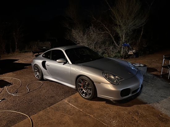 Silver sports car parked on a driveway at night, with trees in the background.