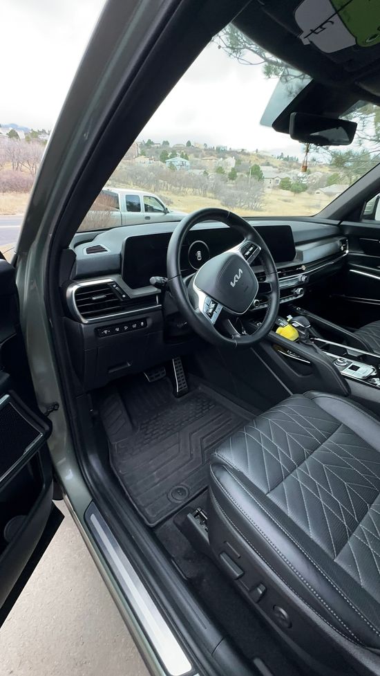 Black car interior with steering wheel, dashboard, and leather seats, viewed from the open driver’s door