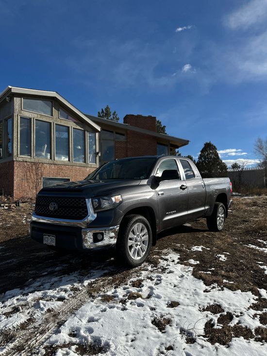 Black pickup truck parked on snowy ground beside a brick house under a blue sky