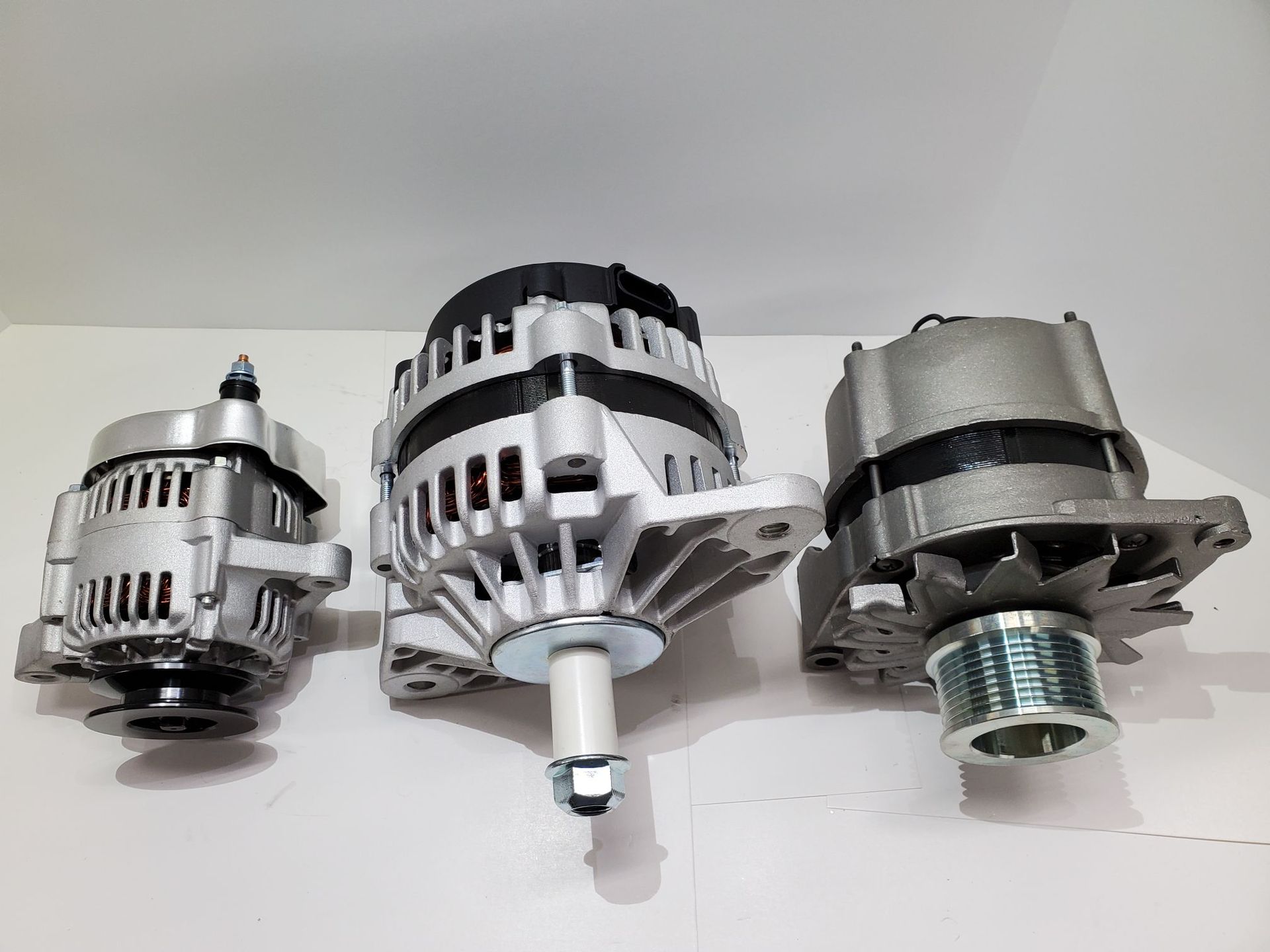 Three silver car alternators displayed side by side on a light surface